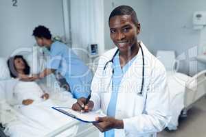 Male doctor writing on clipboard in the ward at hospital
