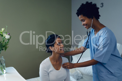 Female doctor examining female patient with stethoscope in the ward