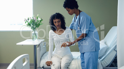 Female doctor helping female patient to get up on hospital bed in the ward