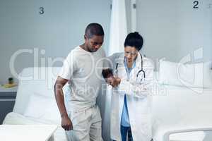 Female doctor helping male patient to walk in the ward