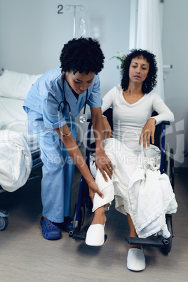 Female doctor helping disabled female patient to move her legs in the ward