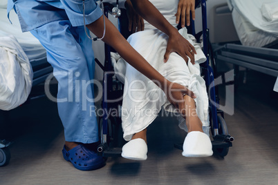 Female doctor helping disabled female patient to move her legs in the ward at hospital