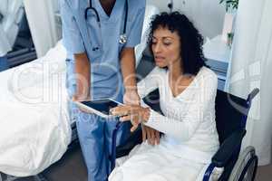 Female doctor helping disabled female patient to use digital tablet in the ward