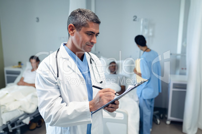 Male doctor writing on clipboard in the ward at hospital