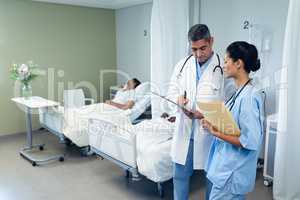 Male and female doctors discussing over clipboard in the ward