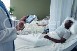 Male doctor looking at x-ray report on digital tablet in the ward