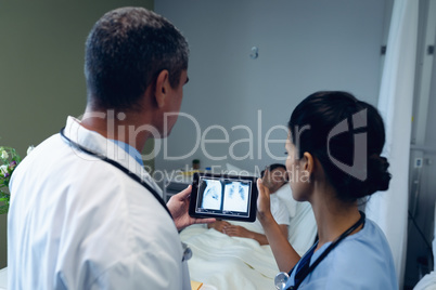 Male and female doctors looking at x-ray report on digital tablet in the ward