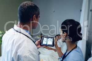 Male and female doctors looking at x-ray report on digital tablet in the ward