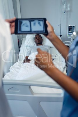 Male and female doctors looking at x-ray report on digital tablet in the ward