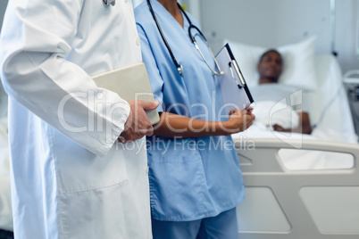 Male and female doctors holding digital tablet and clipboard in the ward at hospital