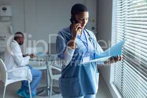Female doctor talking on mobile phone while looking at file
