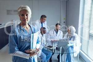 Female surgeon standing with medical file while doctors interacting with each other in the backgroun