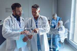 Male doctors discussing over digital tablet at hospital