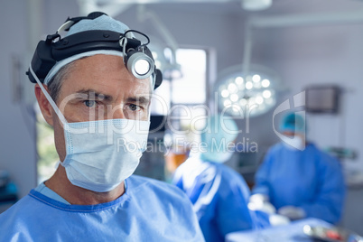 Male surgeon with surgical headlight standing in operation room