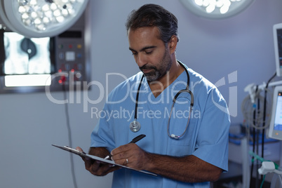 Mature male surgeon writing on clipboard in operation room at hospital