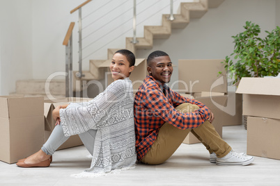 Happy couple sitting back to back in living room at home