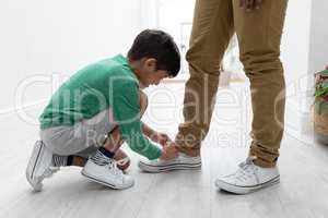 Boy tying his fathers shoelaces at home