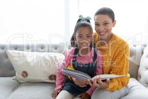 Mother and daughter reading a story book on a sofa in living room at home