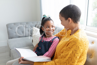 Mother and daughter reading a story book on a sofa in living room