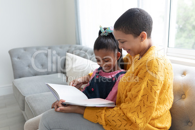 Mother and daughter reading a story book on a sofa in living room