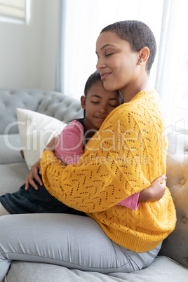 Mother and daughter embracing each other on a sofa in living room