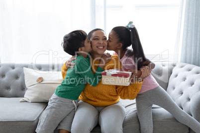Children congratulating mother and giving her gift box in living room