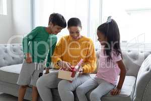 Mother opening a gift box with her children in living room at home