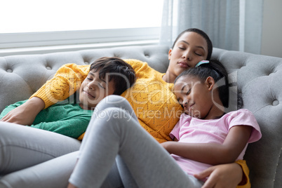 Mother and children sleeping together on a sofa in living room