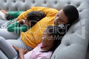 Mother and children sleeping together on a sofa in living room