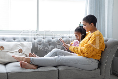 Mother and daughter using digital tablet in living room