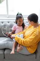 Mother and daughter using digital tablet in living room