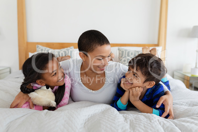 Mother and children relaxing together on bed in bedroom