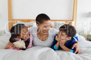 Mother and children relaxing together on bed in bedroom