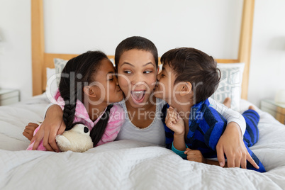 Children kissing their mother on bed in bedroom