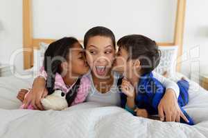 Children kissing their mother on bed in bedroom
