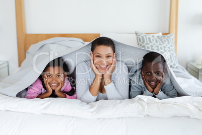 Mother and children relaxing under a blanket in bedroom