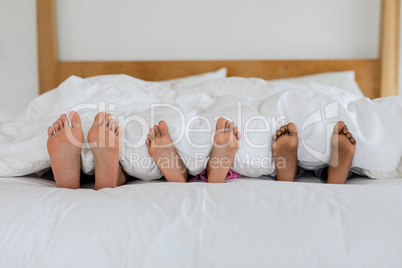 Mother and children sleeping barefoot in bed in bedroom at home