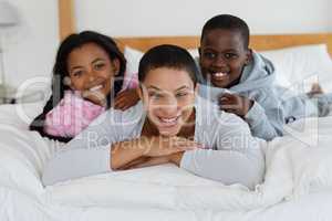 Mother and children relaxing together on bed in bedroom at home