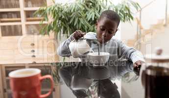 Boy pouring milk in a bowl on dining table