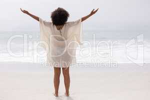 Woman standing with arms outstretched on beach in the sunshine