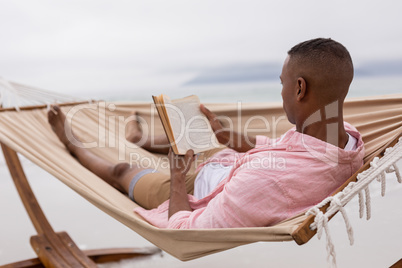 Man reading a book while relaxing on a hammock at beach