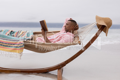 Man reading a book while relaxing on a hammock at beach