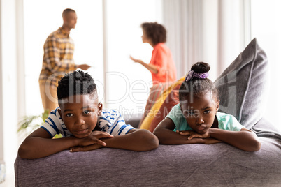 Upset children sitting on a sofa while their parents arguing in the background