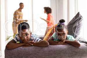 Upset children sitting on a sofa while their parents arguing in the background