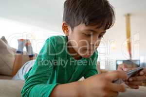 Boy playing game on mobile phone while lying on sofa at home