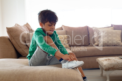 Boy tying shoelace on sofa in living room at comfortable home