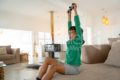 Excited boy playing video game on sofa in living room at comfortable home