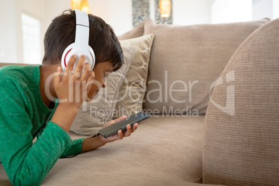 Boy with headset listening music on mobile phone on sofa in a comfortable home