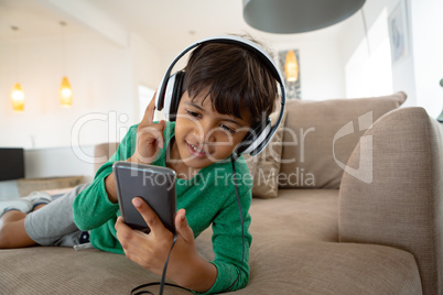 Boy with headset listening music on mobile phone on sofa in a comfortable home