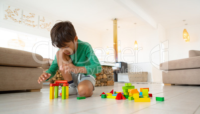 Boy playing with building blocks on floor in living room at comfortable home